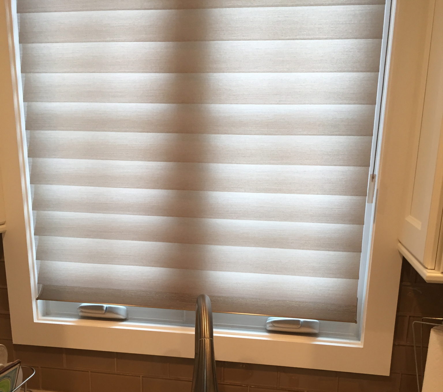 Closed beige blinds on a window above a kitchen sink with a faucet.